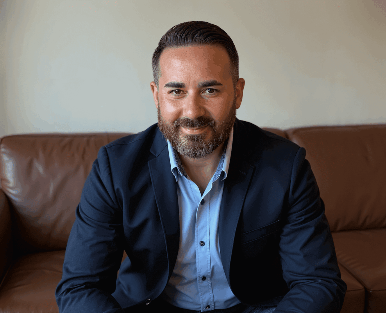 Confident man in a navy suit sitting on a leather couch.