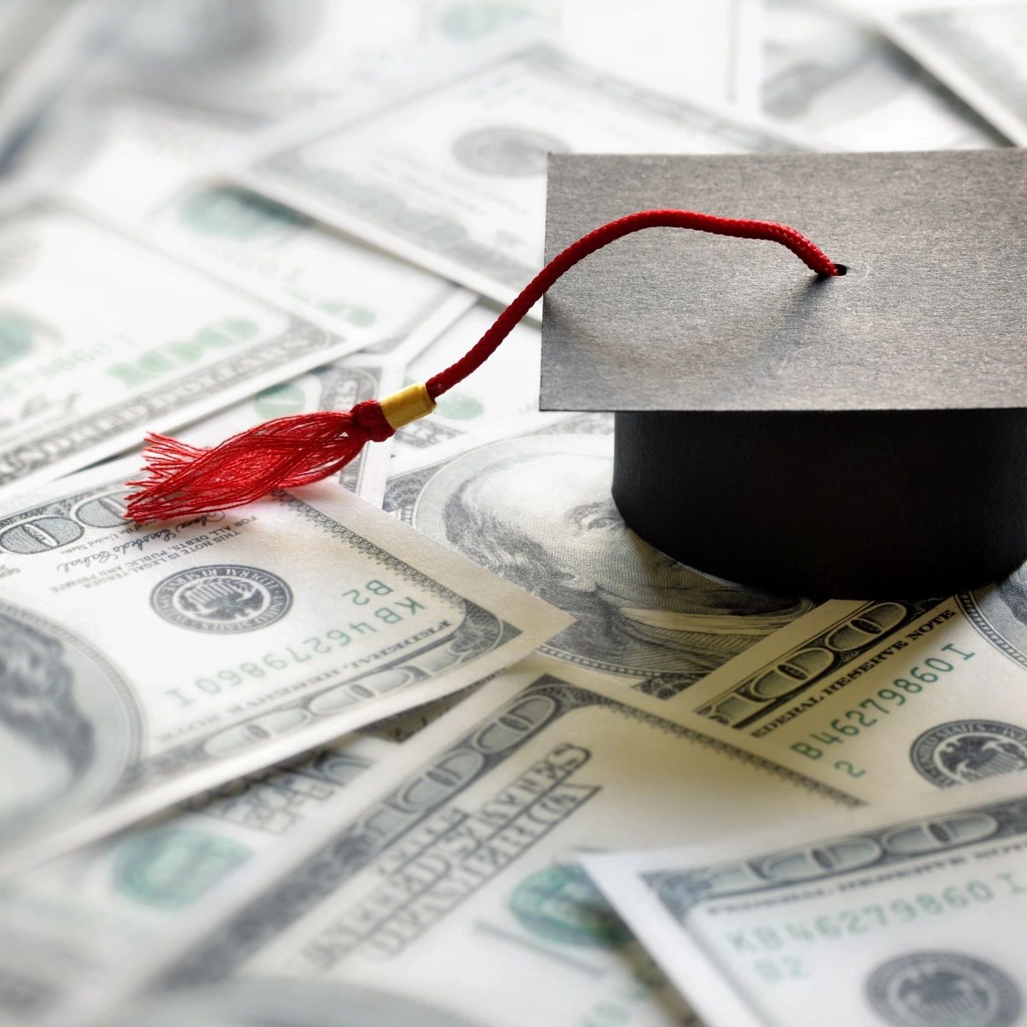 Graduation cap resting on a pile of US dollar bills.